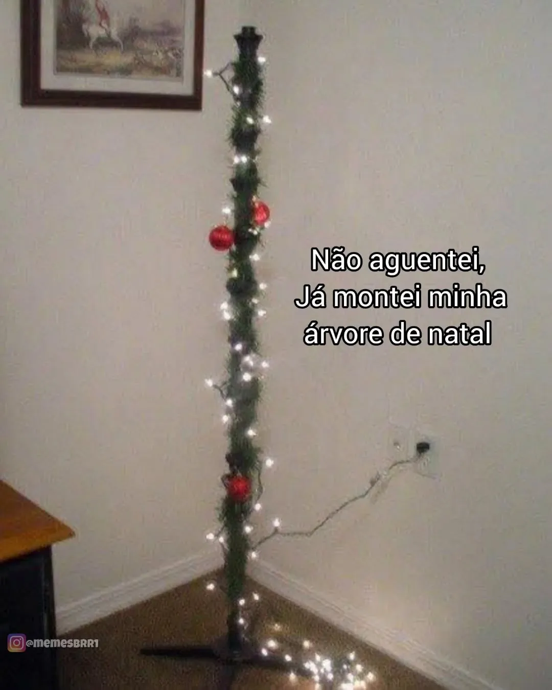 Meme de árvore de Natal improvisada, fina e decorada com luzes e poucas bolas vermelhas no canto da sala.