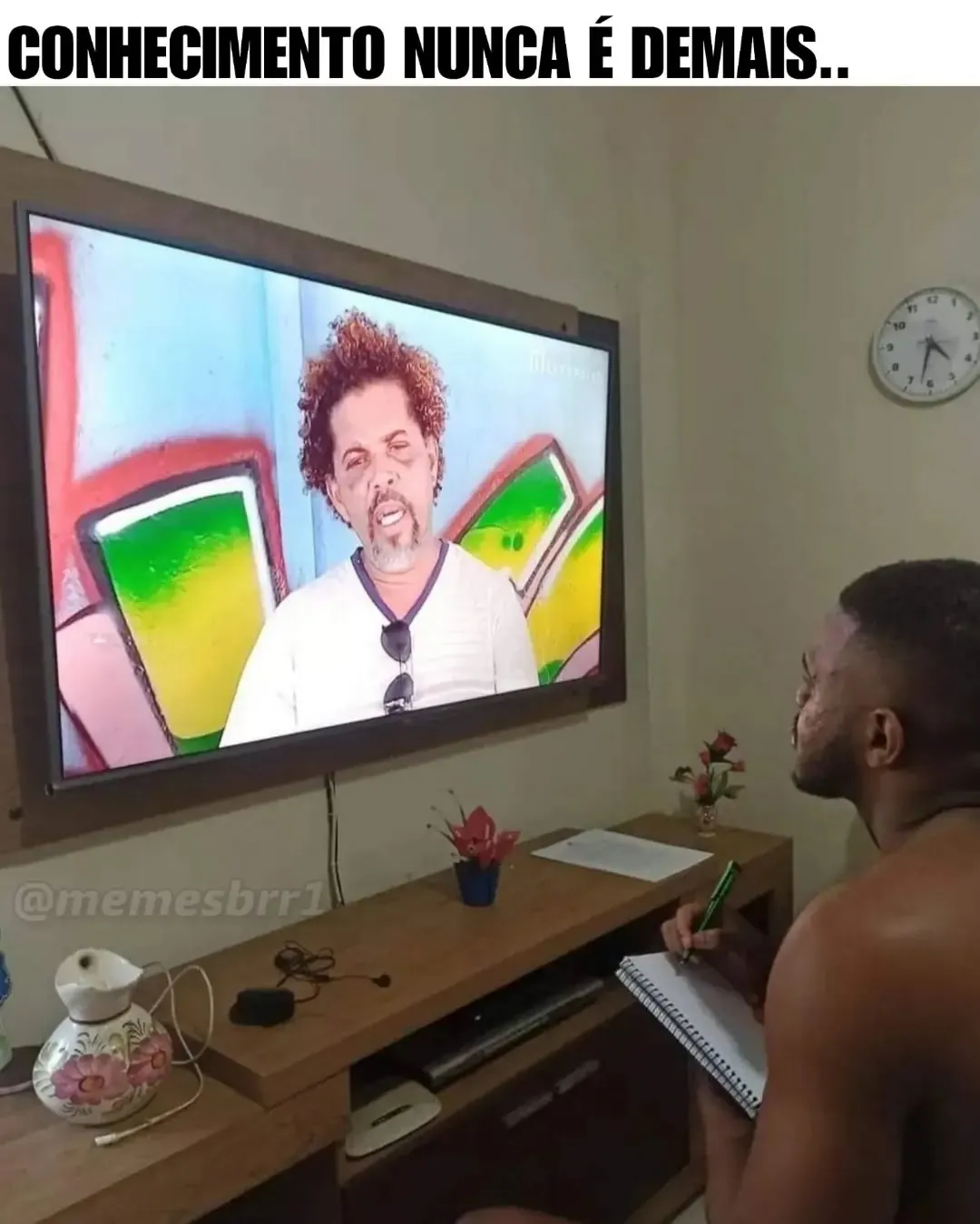 Homem sentado anotando em um caderno enquanto assiste à televisão: conhecimento nunca é demais.
