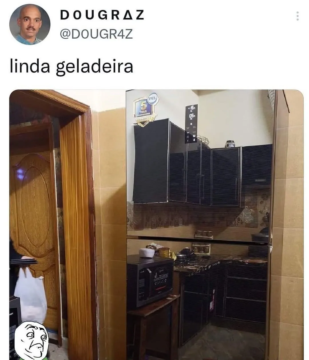 Meme de uma linda geladeira preta e brilhante refletindo toda a cozinha, com troll face no canto.