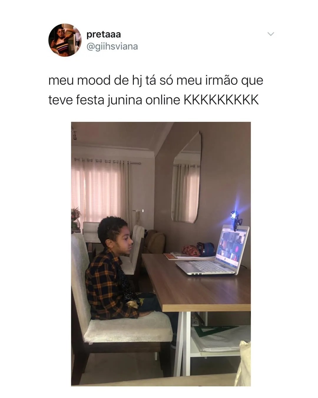 Menino sentado à mesa olhando para um notebook durante uma festa junina online com o irmão.